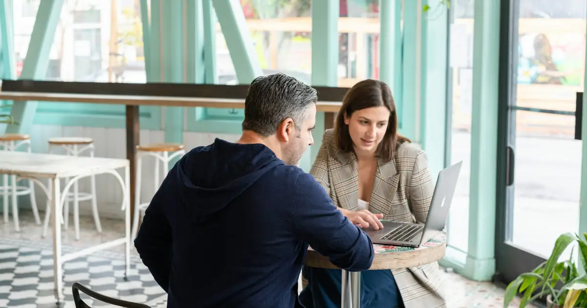 Una diseñadora le muestra un sitio web en la laptop a un cliente, sentados a una mesa de café